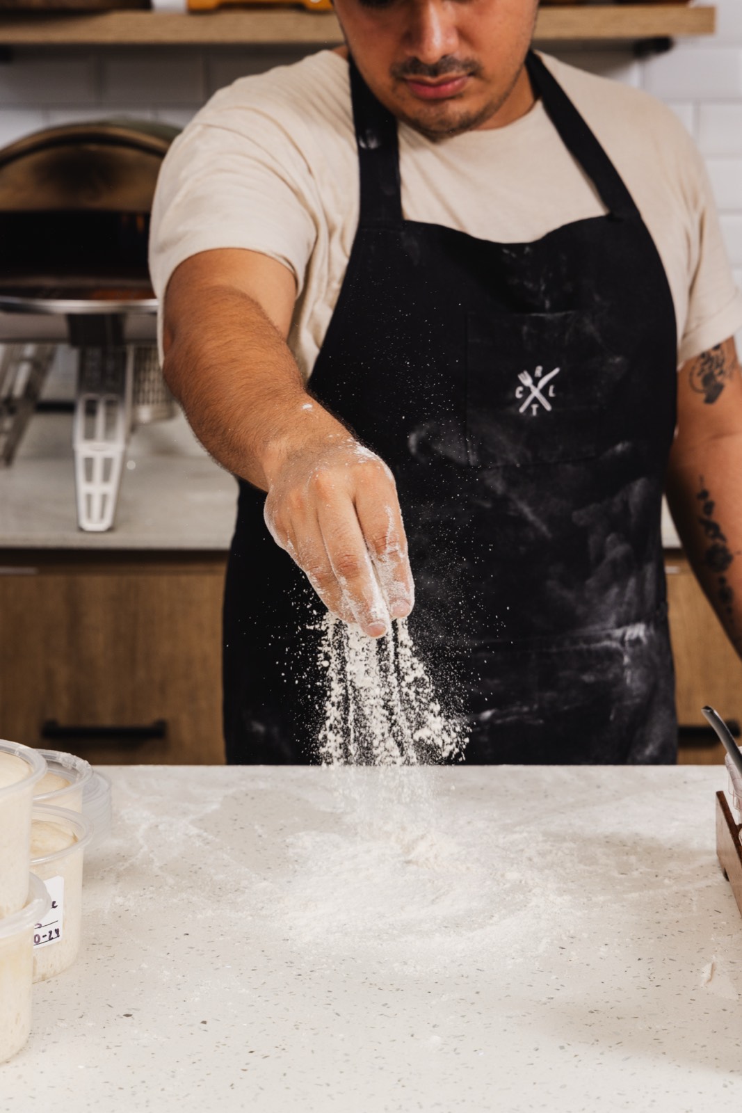 Holy Crust baker dusting flour over sourdough pizza dough