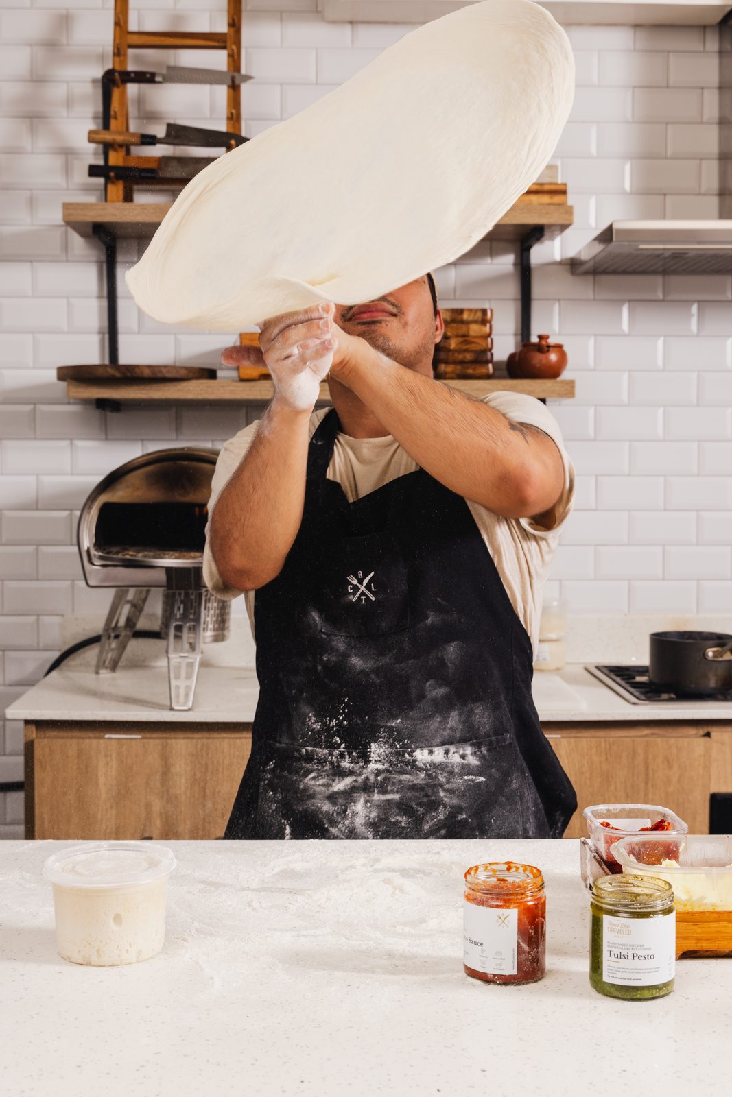 A pizza base stretched in the air over the bench