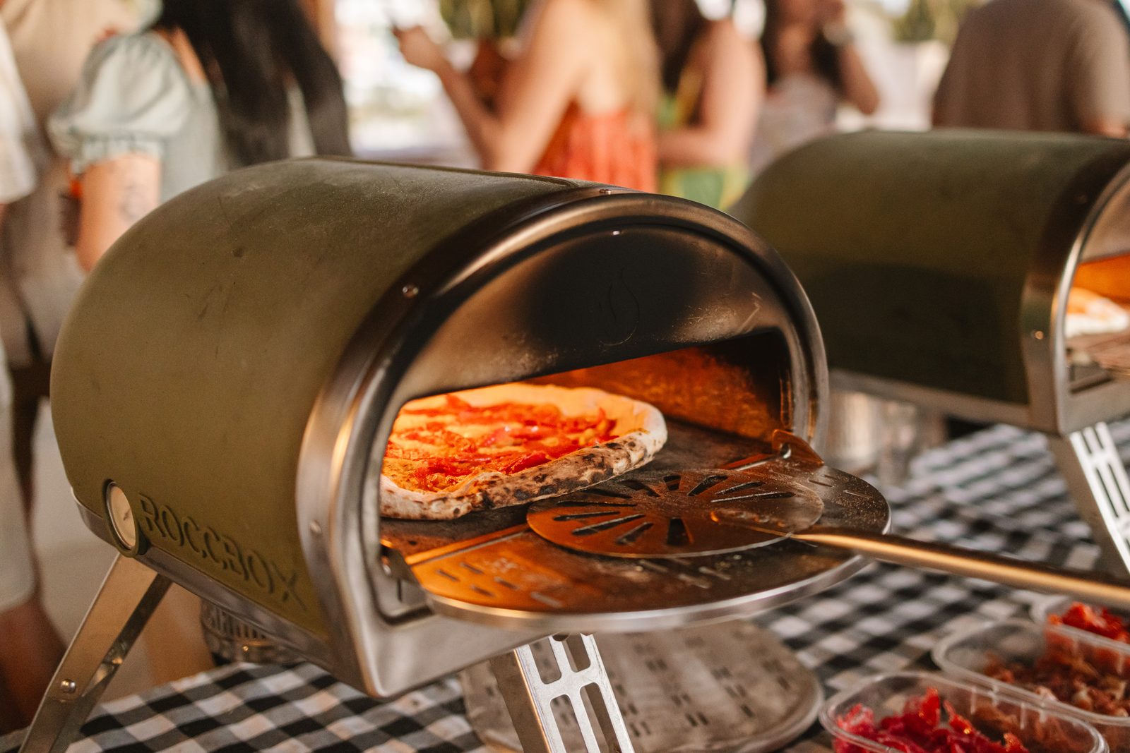 Peel sliding a pizza into the portable oven at an event