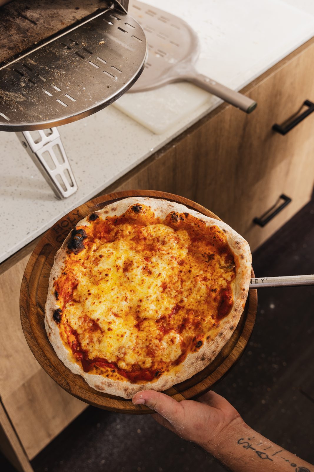 A finished pizza coming out of the oven on the peel